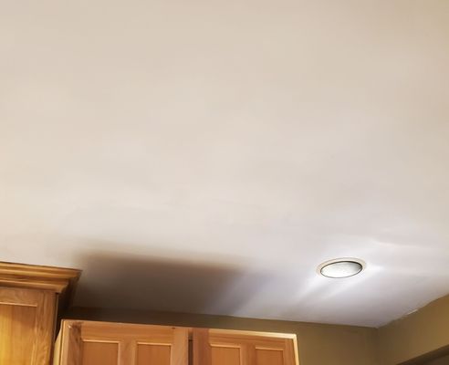 Done Right Drywall — seamlessly repaired kitchen ceiling corner with a new flush-mount recessed light above wood cabinets (after)