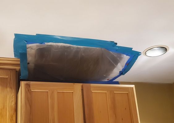 Done Right Drywall — water-damaged kitchen ceiling patch taped off with blue painter tape and plastic sheeting (before)