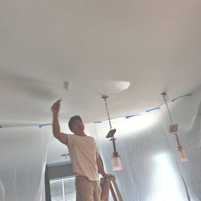 Done Right Drywall — crew member on a ladder rolling a finish coat on a living-room ceiling with pendant lights wrapped in plastic
